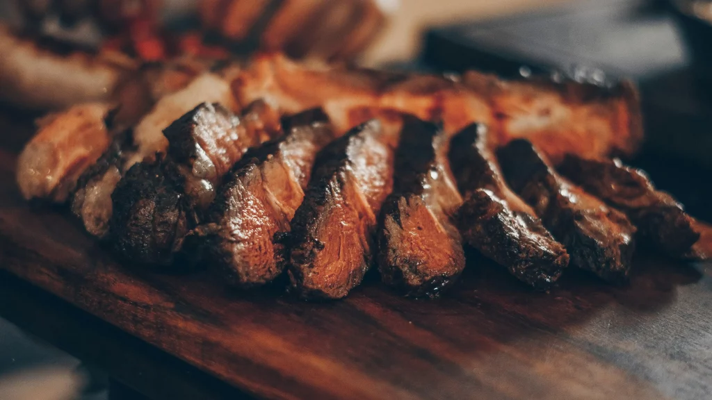 Picanha fatiada e grelhada, servida em uma tábua de madeira. Carne suculenta com bordas douradas e crocantes, destacando o ponto ideal de cozimento.