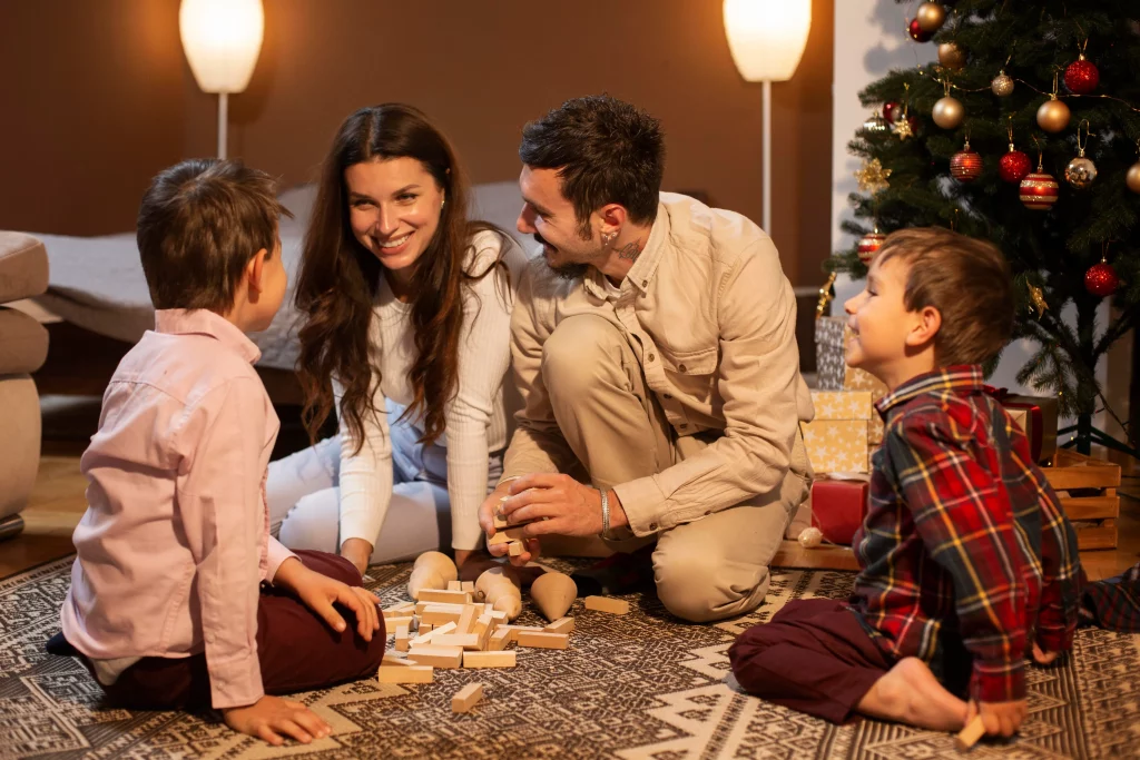 Família sorridente reunida brincando com jogos de tabuleiro ao lado de uma árvore de Natal decorada.