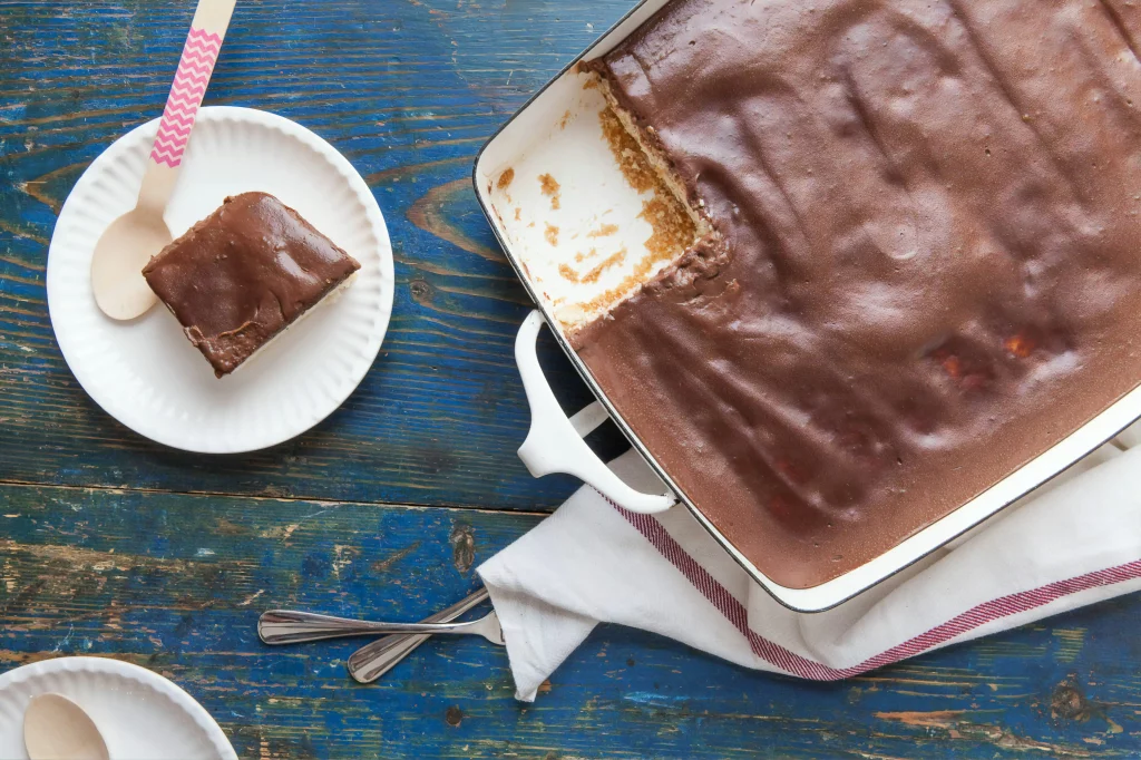 Travessa de pavê de chocolate com uma fatia servida em prato branco, mostrando camadas de biscoito e creme de chocolate.