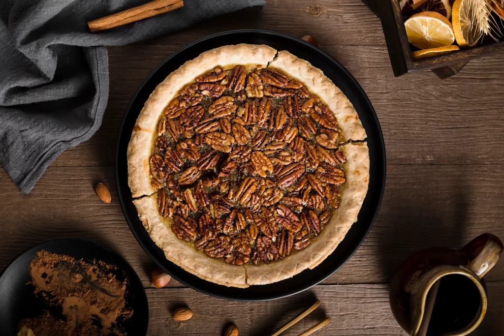 Torta de nozes pecan com massa dourada e recheio caramelizado, servida em prato preto e decorada com canela.