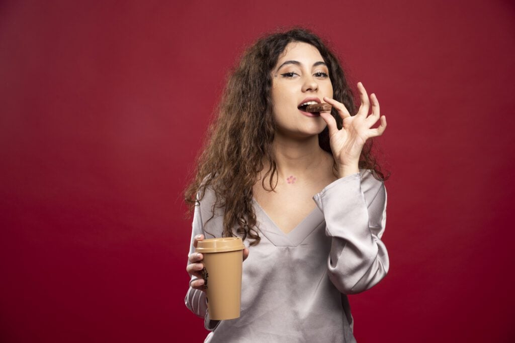 Mulher comendo chocolate enquanto segura um copo de café