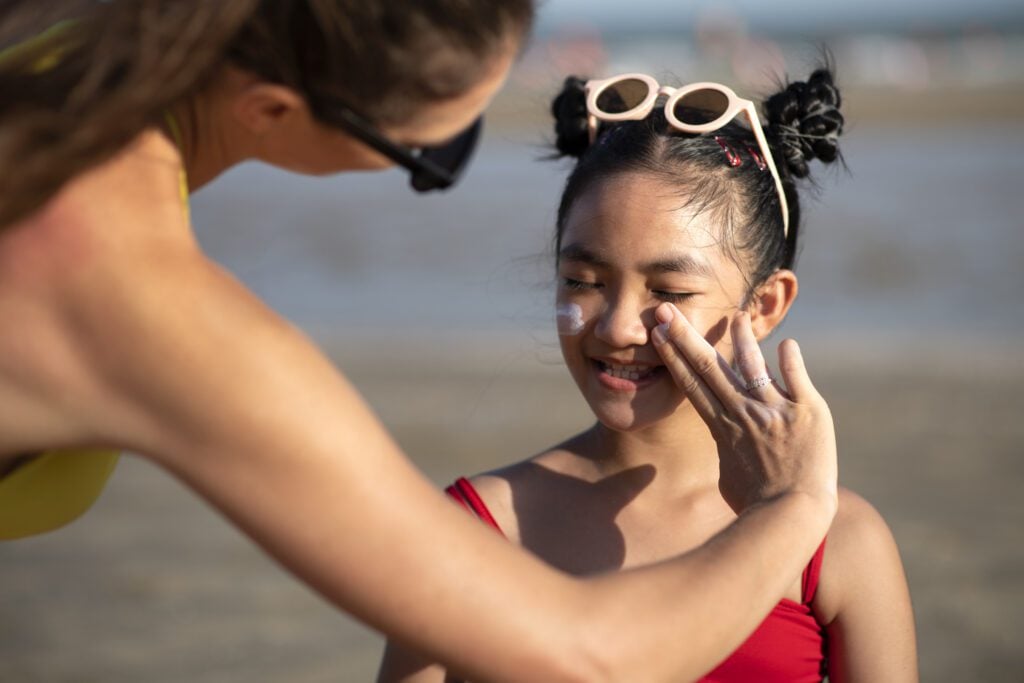 Mãe passando protetor solar facial em sua filha